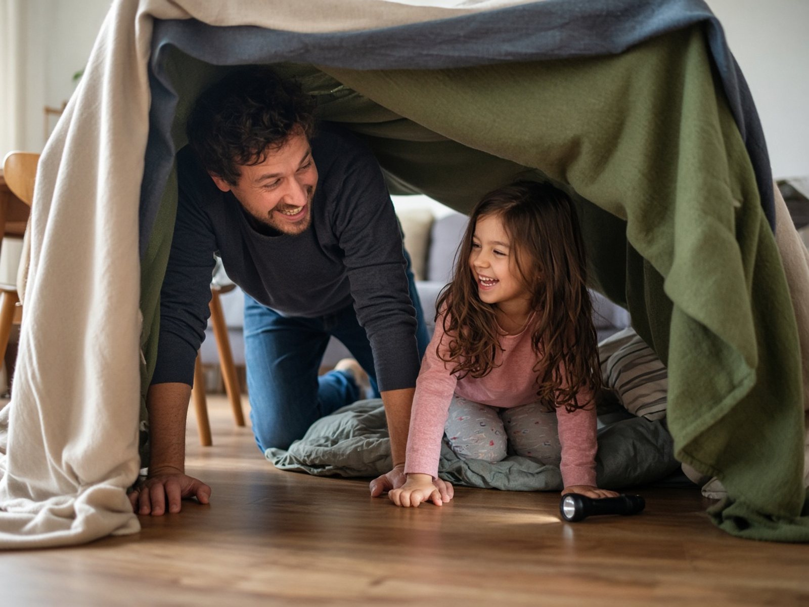 A father and daughter build a blanket fort in a living room